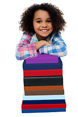 Image showing Smart little girl leaning over pile of books