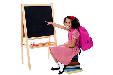 Image showing Cute smiling student pointing at blank chalkboard