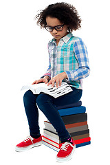 Image showing Young kid sitting on stack of books and reading