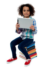 Image showing Adorable kid with tablet pc sitting on books