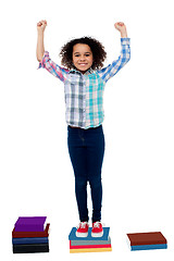 Image showing Excited pretty school child standing on books