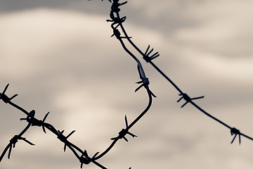 Image showing Barbed wire against moody sky. Toned shot, closeup.