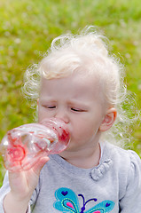 Image showing The small blond girl drinks water from a bottle, a close up