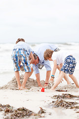 Image showing father and sons on the beach playing in the sand