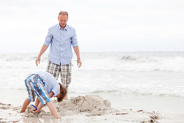 Image showing father and sons on the beach playing in the sand