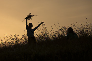 Image showing Silhouettes of girl picking flowers during midsummer soltice 