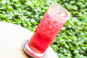 Image showing Glass of iced sweet red drink on green background