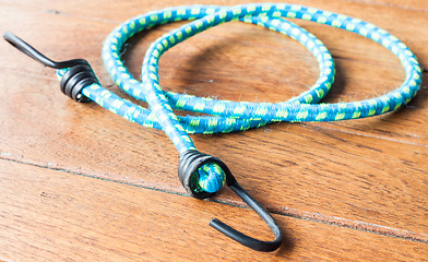 Image showing Blue elastic rope with metal hooks on wood background