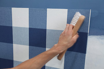 Image showing decorator hanging wallpaper with work tool in motion