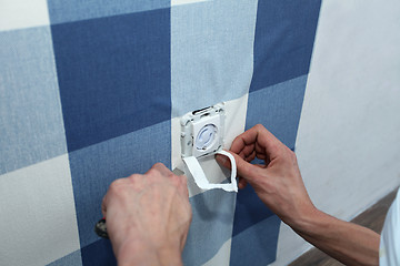 Image showing decorator with scalpel hanging wallpaper over wall socket   