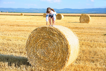 Image showing small rural girl on the straw after harvest field with straw bal