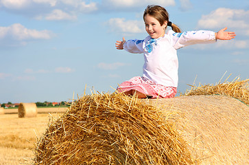 Image showing small rural girl on the straw after harvest field with straw bal