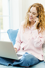 Image showing Woman talking on phone and using computer