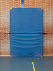 Image showing Large blue mat strapped to a brick wall