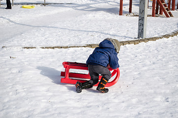 Image showing boy with blue jacket knelt down to red sleigh  