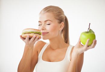 Image showing woman smelling hamburger and holding apple