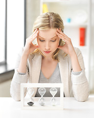 Image showing tired woman behind the table with hourgalss