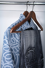 Image showing Blue jeans and shirts on wooden hangers