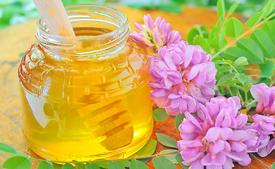 Image showing glass jar full of honey and stick with acacia pink and white flo