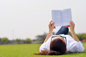 Image showing Young woman reading a book in the park