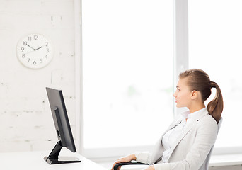 Image showing businesswoman looking at wall clock in office