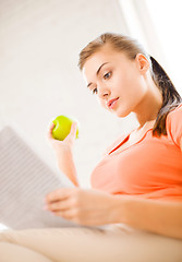 Image showing woman with green apple reading newspaper at home