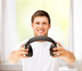 Image showing young smiling man offering headphones at home