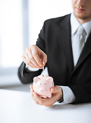 Image showing man putting coin into small piggy bank