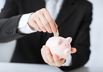 Image showing man putting coin into small piggy bank