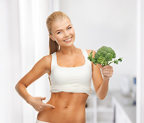 Image showing woman pointing at her abs and holding broccoli