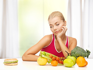 Image showing doubting woman with fruits and hamburger