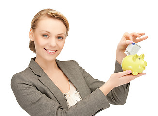 Image showing woman putting cash money into small piggy bank