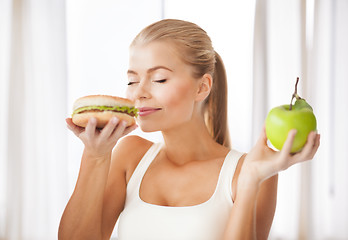 Image showing woman smelling hamburger and holding apple