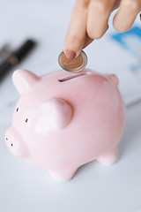 Image showing woman hand putting coin into small piggy ban