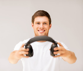 Image showing young smiling man offering headphones