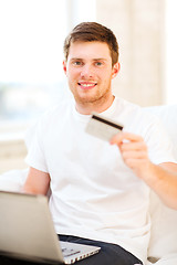 Image showing man with laptop showing credit card at home