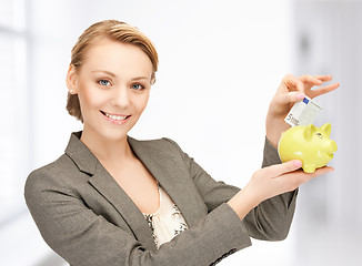 Image showing woman putting cash money into small piggy bank