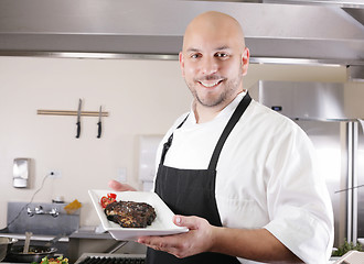 Image showing young male chef presenting a juicy ribeye steak with tomatoes