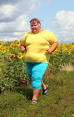 Image showing overweight woman running along field of sunflowers