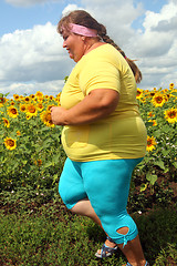 Image showing overweight woman running along field of sunflowers