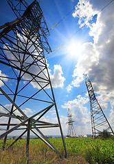 Image showing tall electric masts against sun and sky