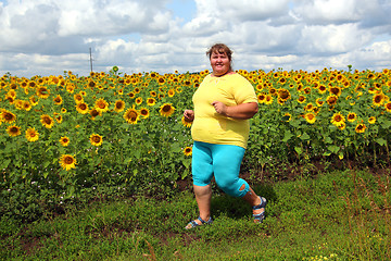 Image showing overweight woman running along field of sunflowers