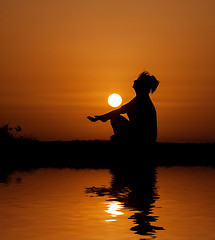 Image showing Silhouette woman sitting and relaxing against orange sunset