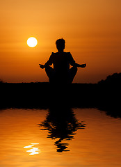 Image showing Silhouette woman sitting and relaxing against orange sunset