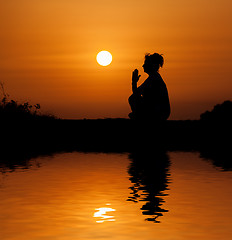 Image showing Silhouette woman sitting and relaxing against orange sunset