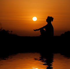 Image showing Silhouette woman sitting and relaxing against orange sunset