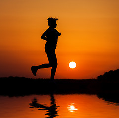 Image showing Silhouette woman running against orange sunset