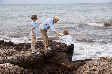 Image showing happy family sitting on rock and watching the ocean waves