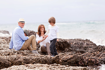 Image showing happy family sitting on rock and watching the ocean waves