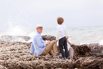 Image showing happy family sitting on rock and watching the ocean waves